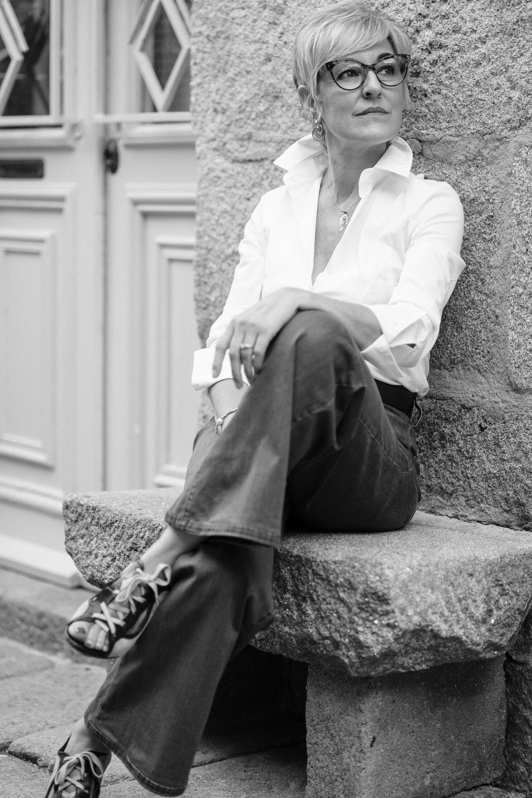 Foto de Sira Domarco en blanco y negro sentada en el banco de piedra junto a su tienda